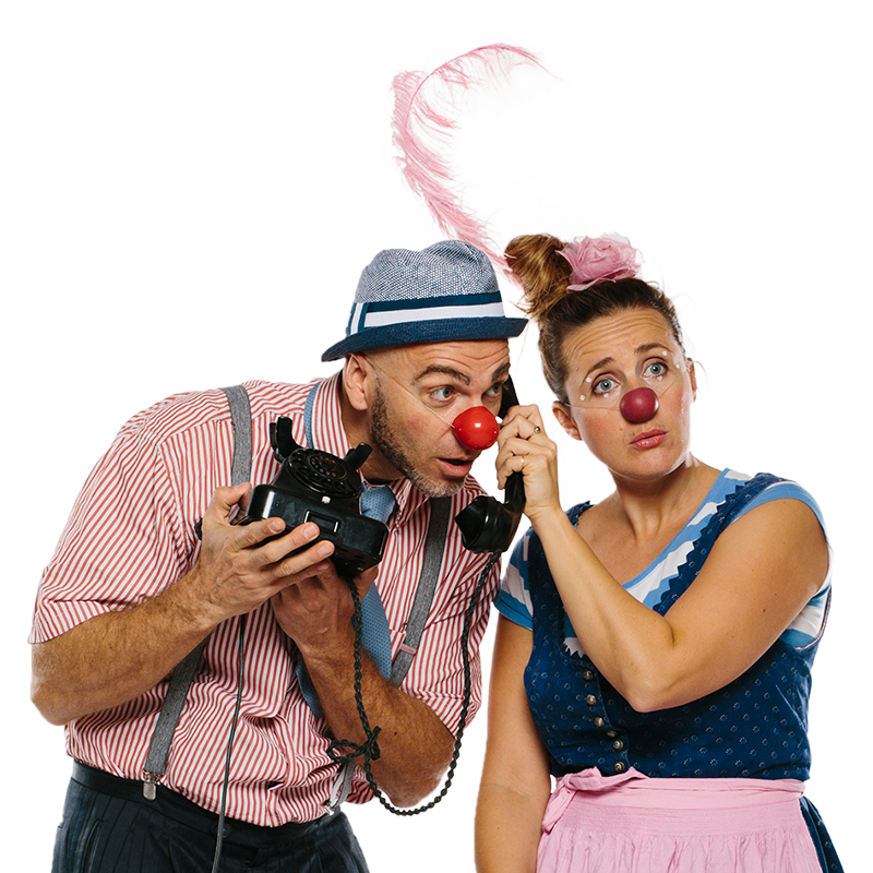Zwei Clowns stehen nebeneinander während der eine eine alten Telefonapparat in der Hand hält und die andere ihm den Hörer hinhält zum Telefonieren